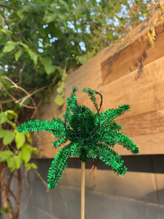 Green decorative palm tree on a stick against a wooden wall and green foliage background