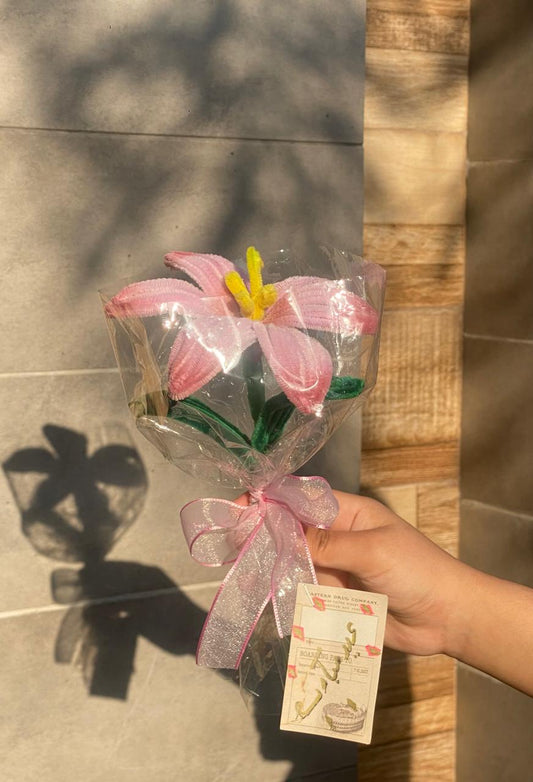 Bouquet of pink flowers wrapped in clear plastic with a pink ribbon, held by a hand against a tiled wall.